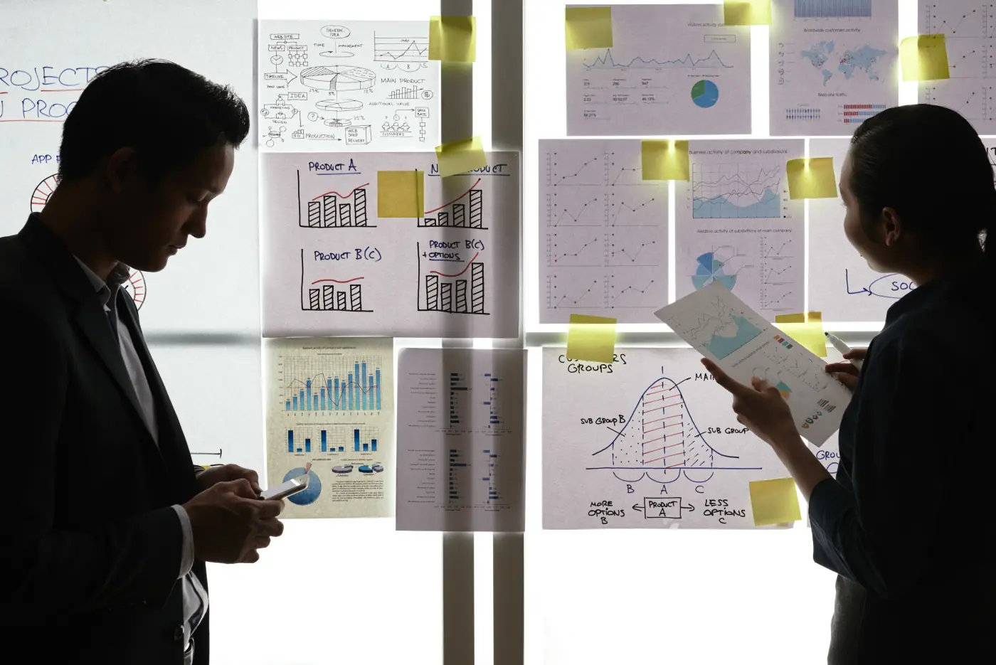 Colleagues standing by window reviewing charts and diagrams